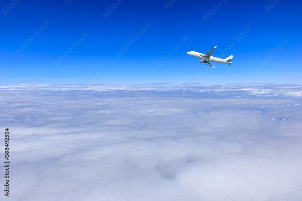 Commercial airplane flying above blue sky and white clouds.