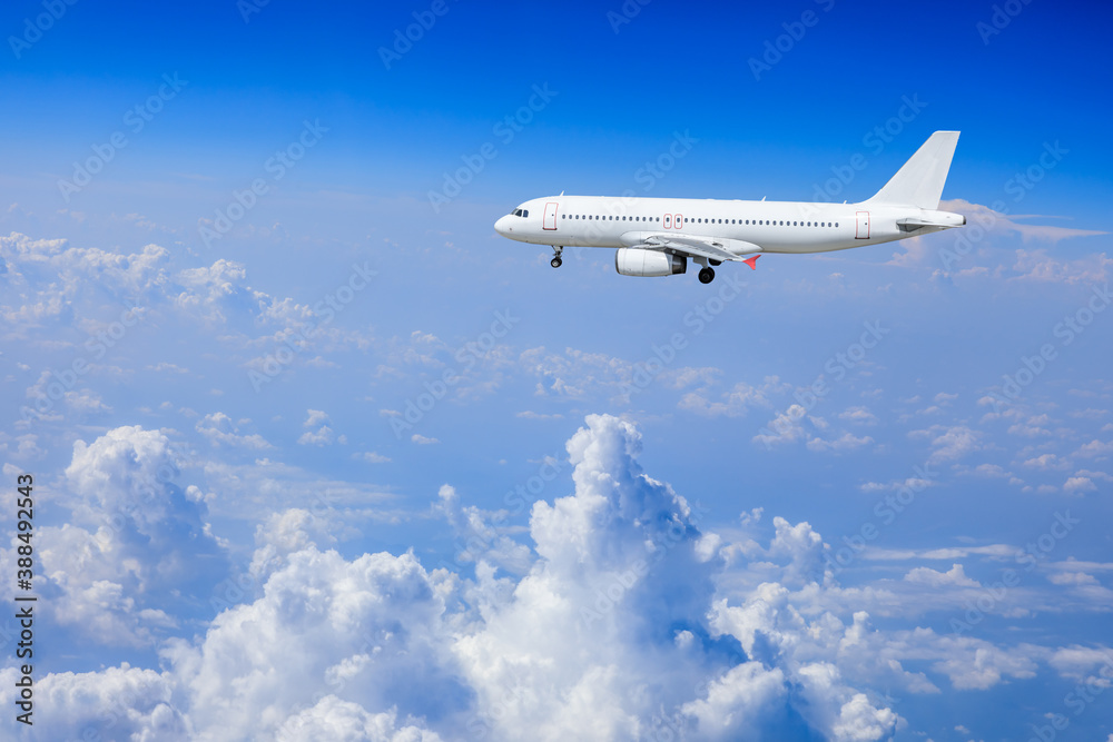 Commercial airplane flying above blue sky and white clouds.