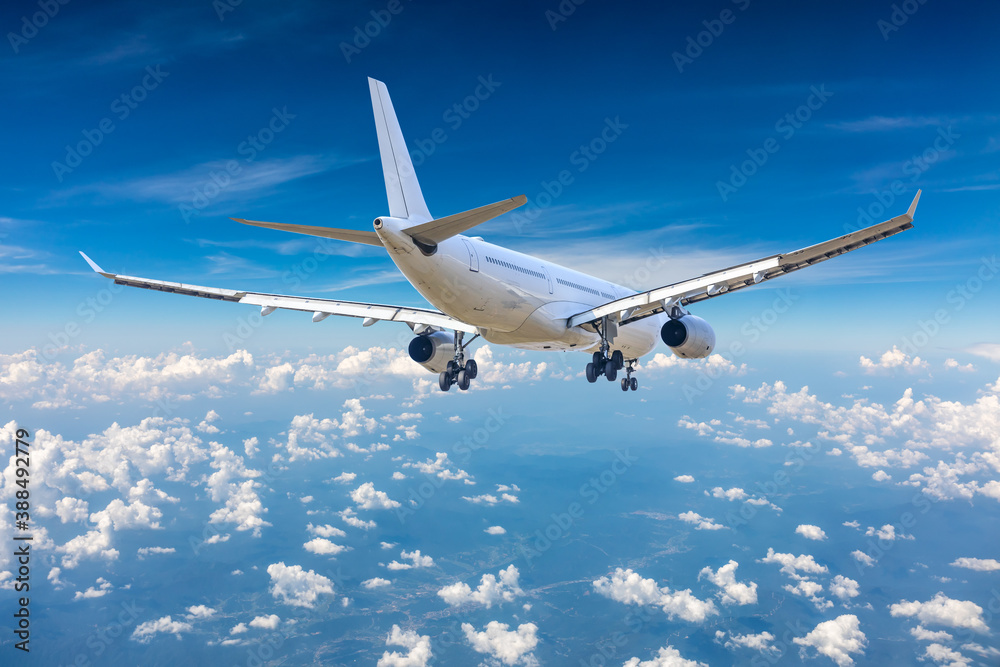 Commercial airplane flying above blue sky and white clouds.