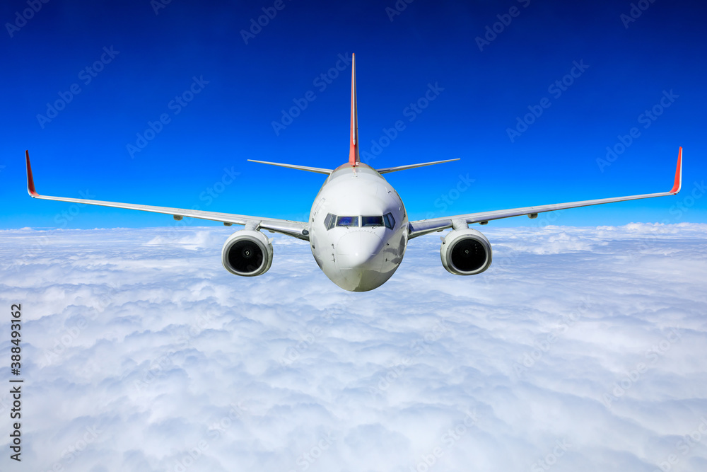 Commercial airplane flying above blue sky and white clouds.