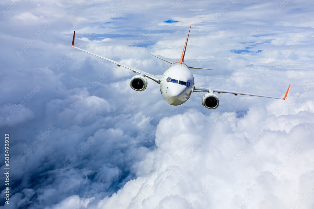 Commercial airplane flying above blue sky and white clouds.