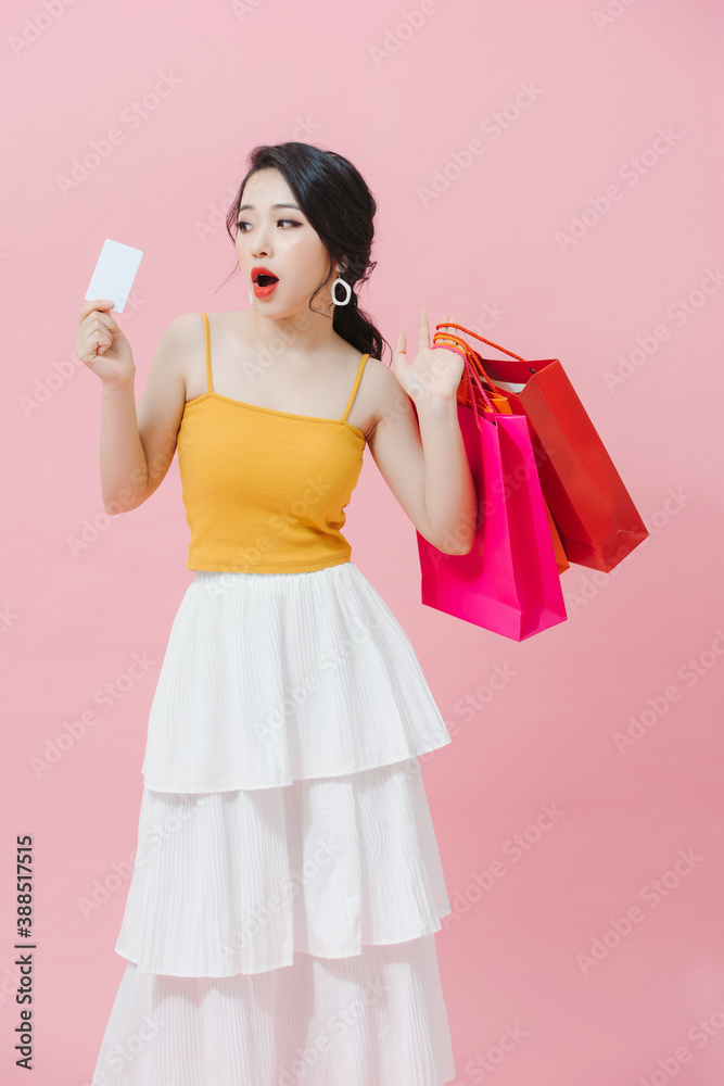 Pretty Asian woman is showing credit card in her hand along with several shopping bags in another ha