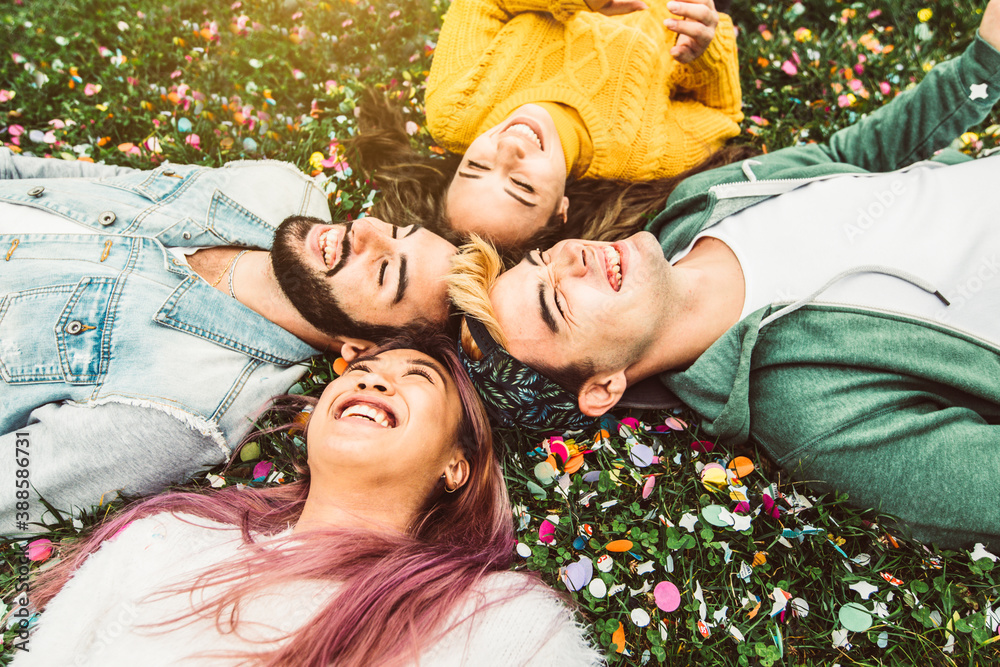 Group of multiracial friends having fun lying on the grass - Young people laughing outdoor at the pa