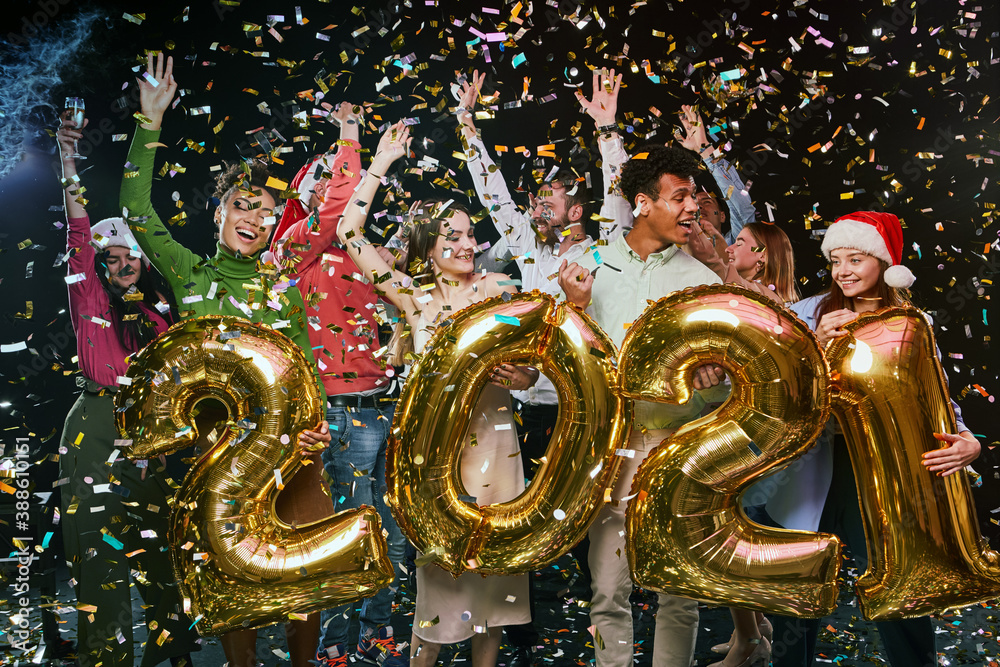 New Year Party with friends. Group of young happy multiracial people holding golden foil balloons in