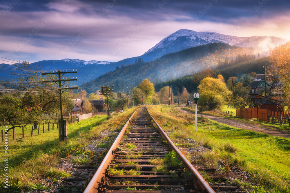 Railroad in mountains with snowy peaks at sunset in autumn. Industrial landscape with railway statio