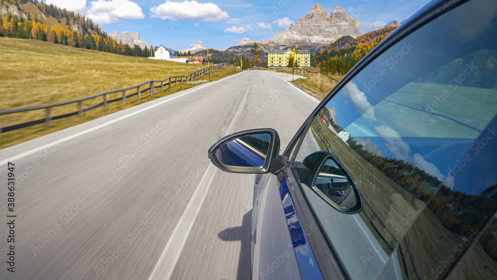 CLOSE UP: Shiny blue car drives along empty road leading to town of Misurina.