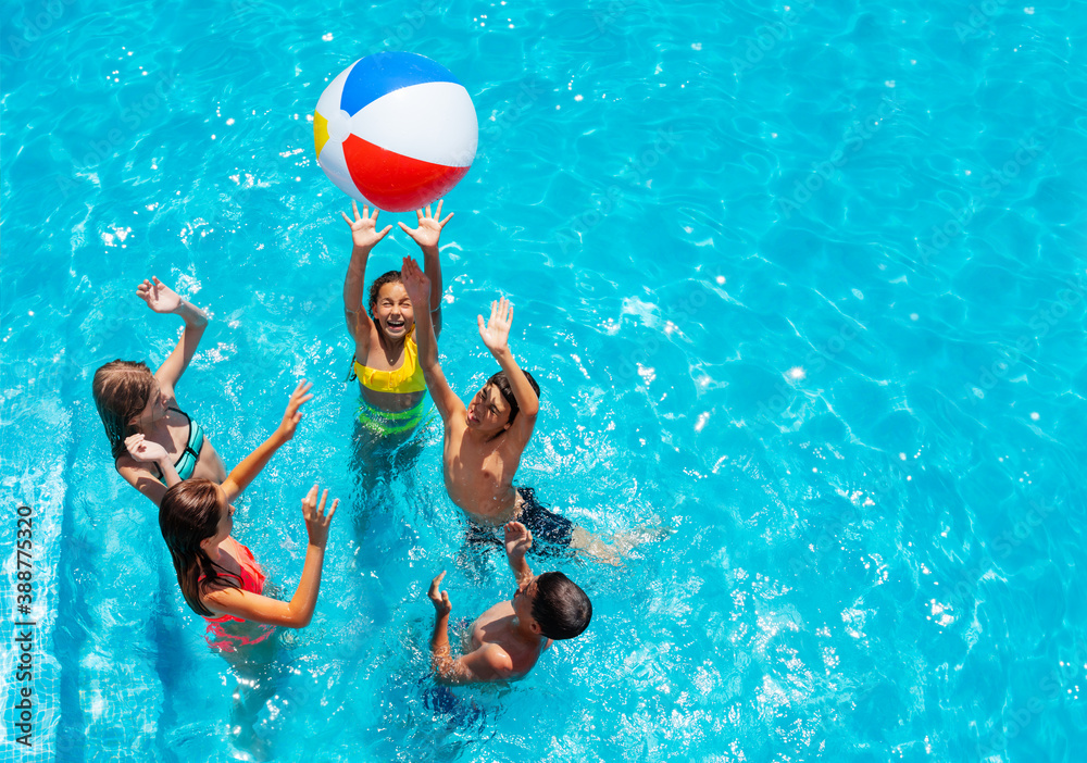 Group of kids in swimming pool play with inflatable ball view from above reaching hands up