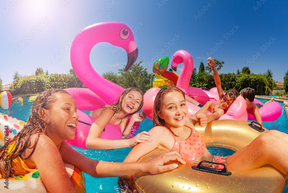 Many laughing girls swim and float on inflatable toy in a group of friends in swimming pool outside 