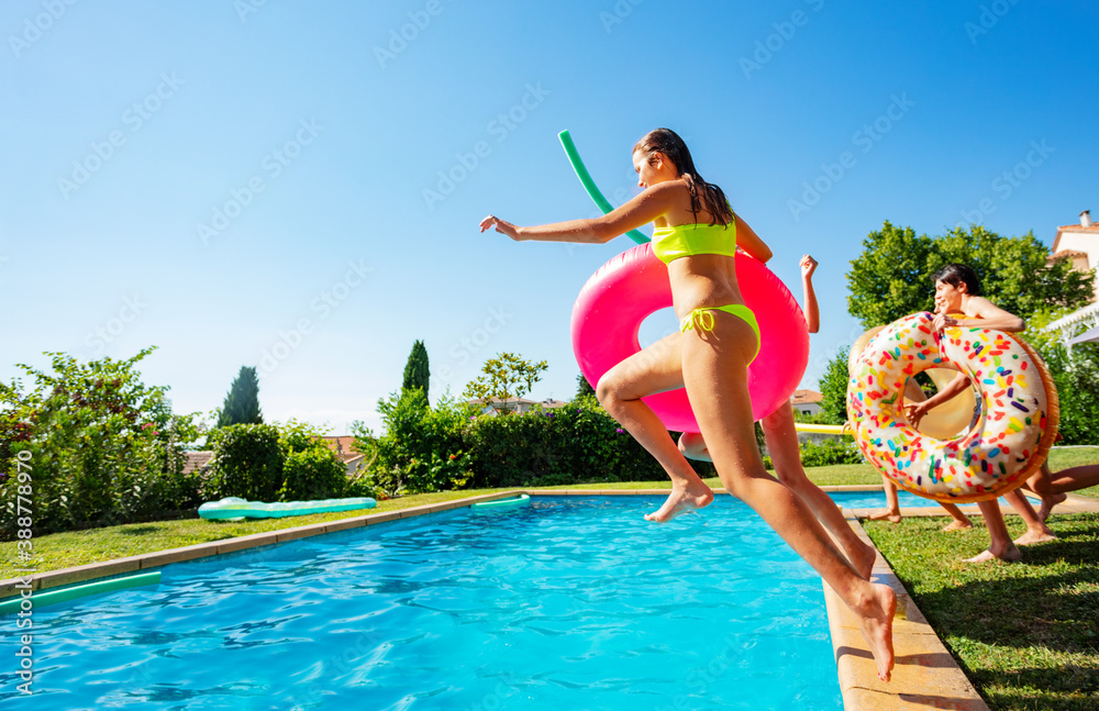 Group of happy teenage kids with inflatable buoys jump into pool jumping together view from side