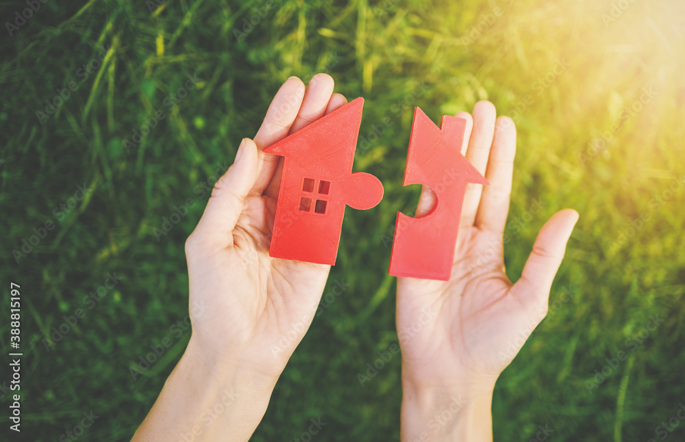 Red house with a shape of two parts of puzzle in human hands.