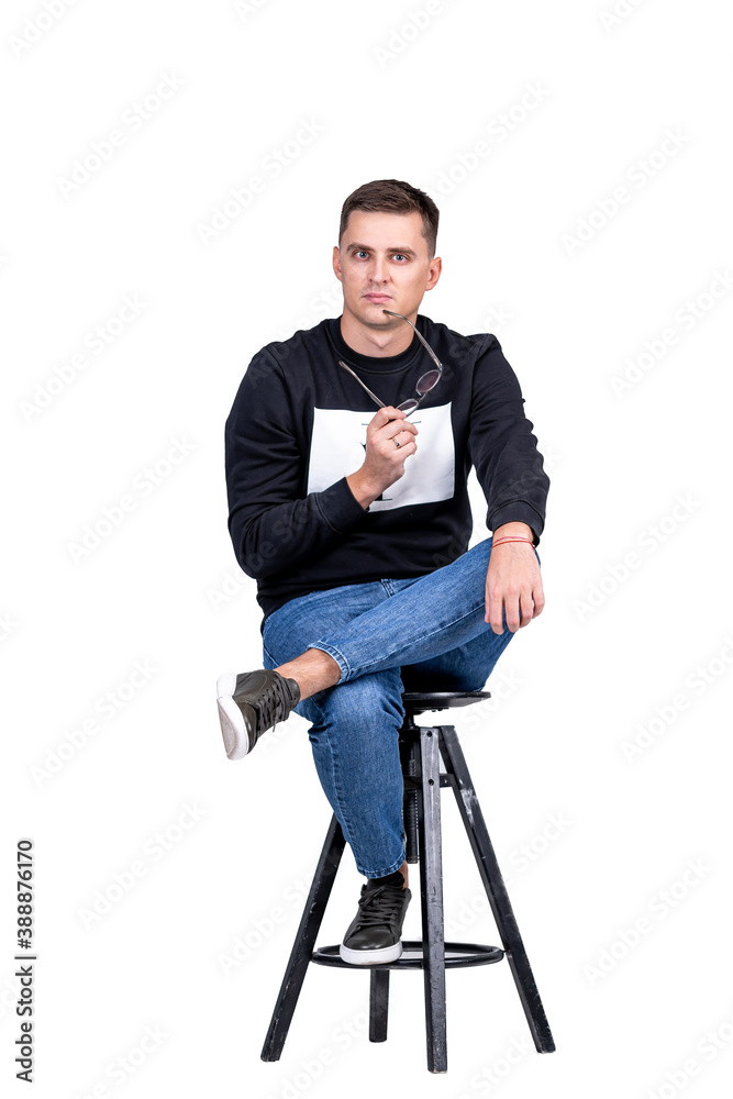 Man in casual clothes holds glasses in hands. Casual clothes and high bar chair. White background.