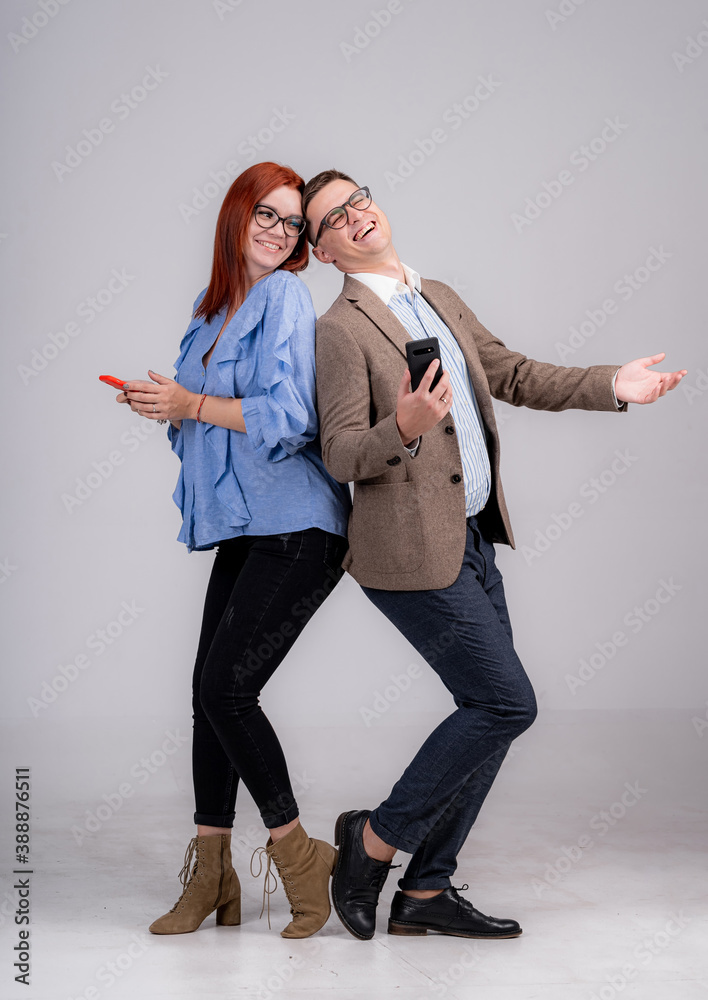 Full length photo of a young casual couple standing back to back and looking into the camera. White 