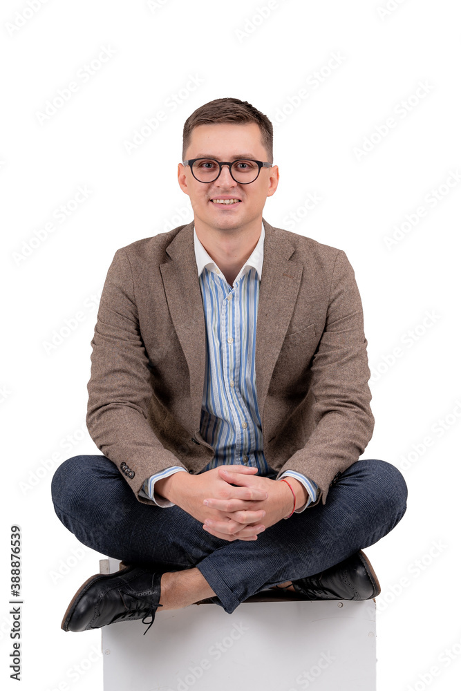 Smart smiling guy sitting on the floor with crossed legs. White background. Male in suit.