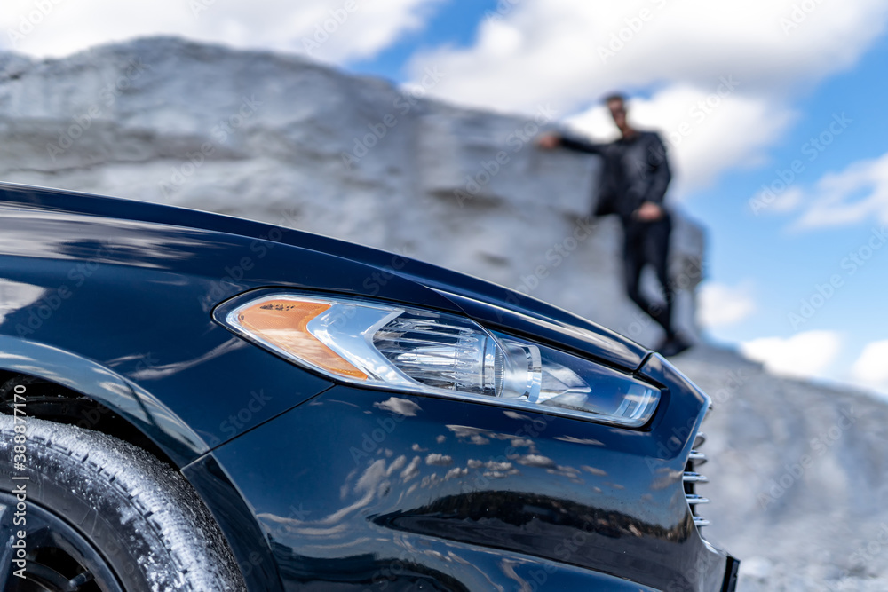 Black luxury car on front view. White quarry background. Stylish man stands on the rock on the backg