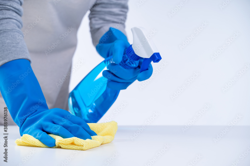 Woman housekeeper using rag and spraying bottle to clean the table surface.