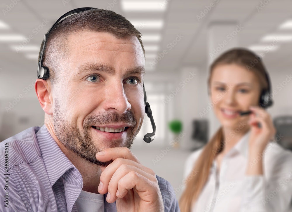 A smiling young businessman call center agent wears a wireless headset at the workplace.