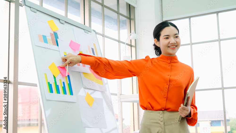 Young woman explains business data on white board in casual office room . The confident Asian busine