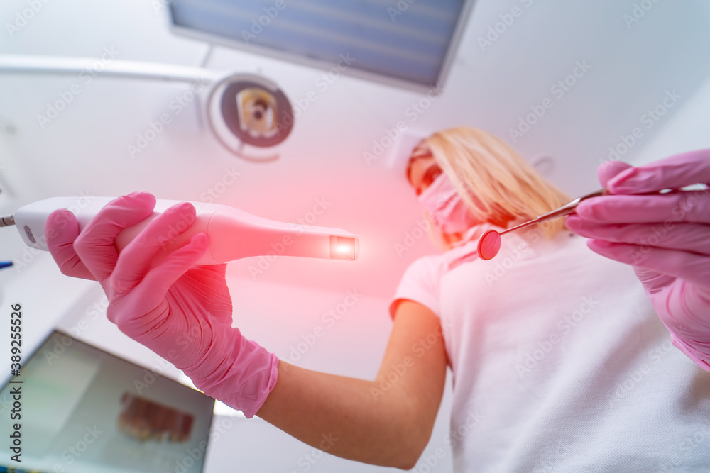 Pink medical gown mask on the face of a woman doctor. Tools for examining the oral cavity in hands. 