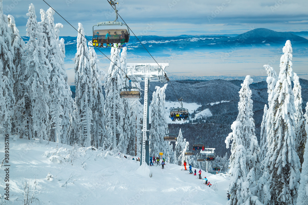 Ski lifts with skiers in the snowy pine forest, Romania