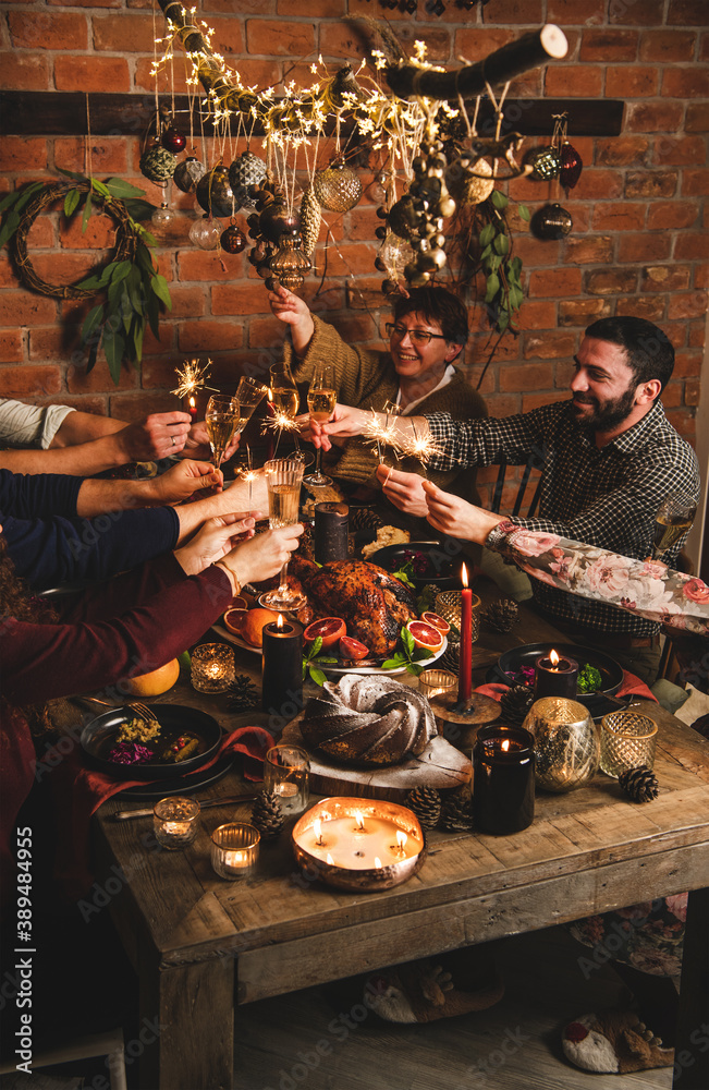 Friends or family burning sparklers and feasting over table with whole roasted turkey with rice, cho