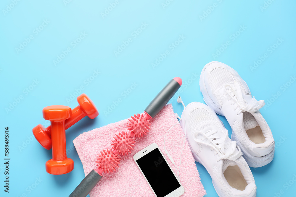 Body roller with shoes, towel, mobile phone and dumbbells on color background