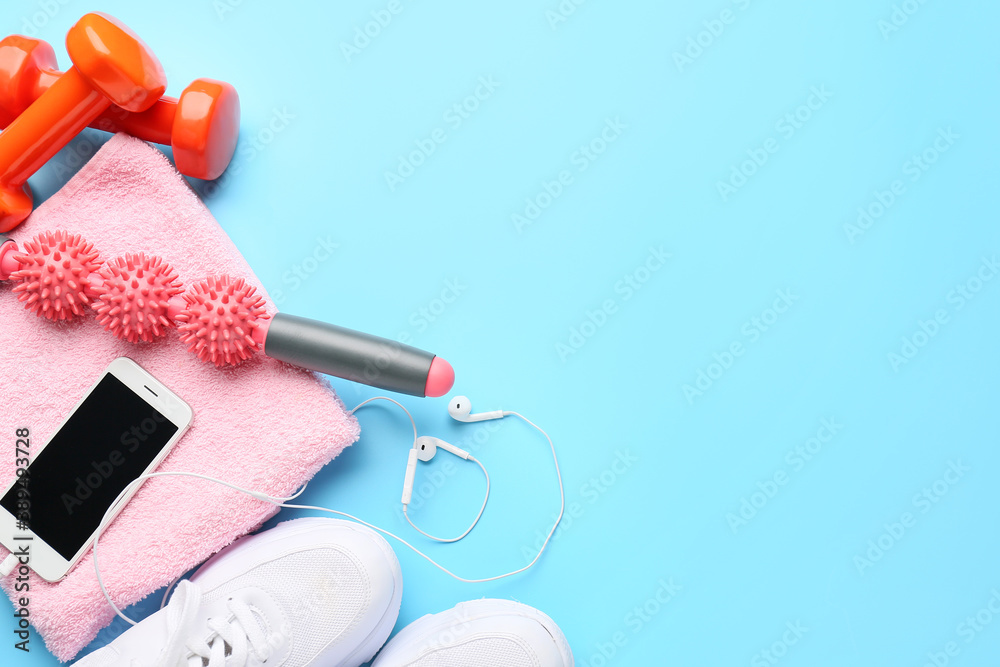 Body roller with shoes, towel, mobile phone and dumbbells on color background