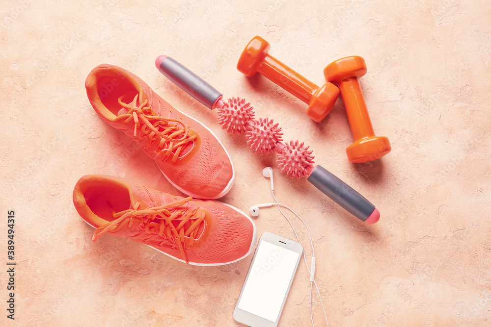 Body roller with shoes, dumbbells and mobile phone on color background