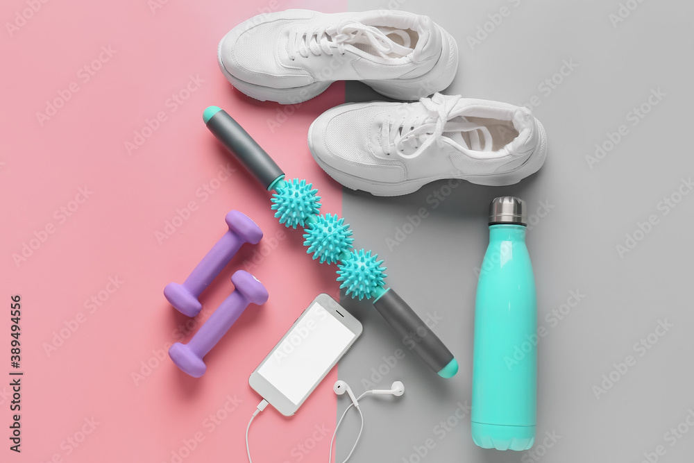 Body roller with shoes, dumbbells, bottle of water and mobile phone on color background