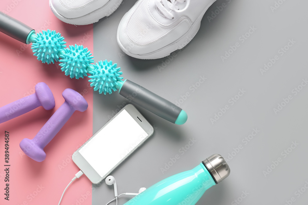 Body roller with shoes, dumbbells, bottle of water and mobile phone on color background