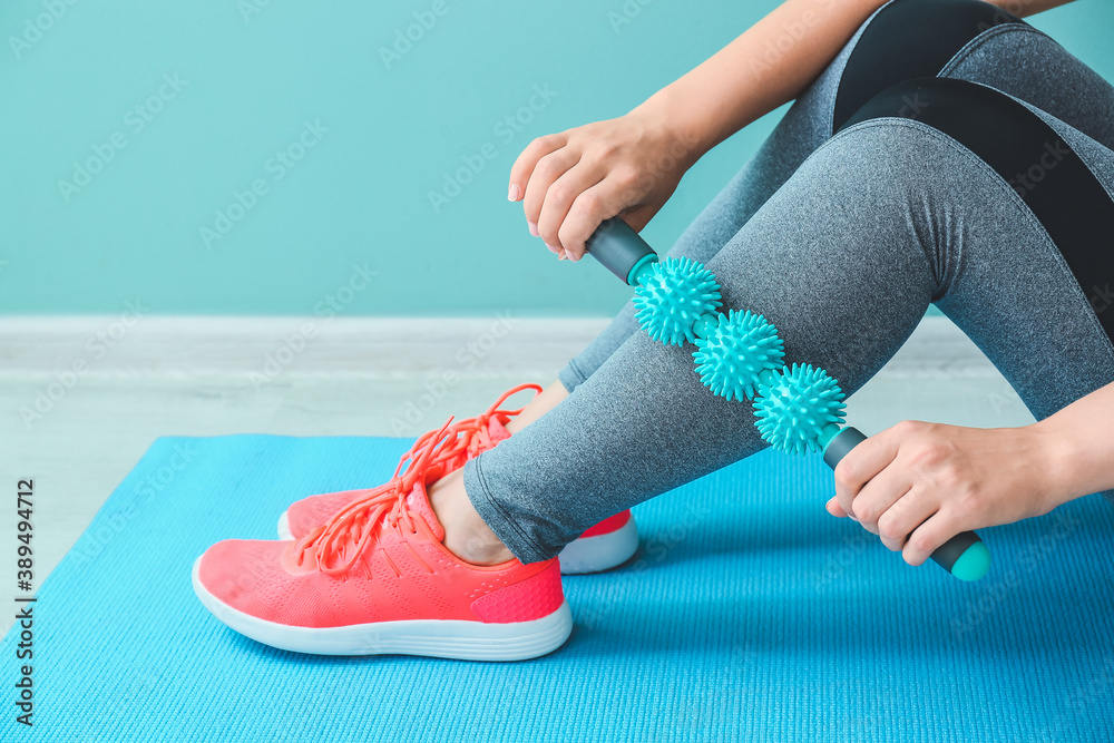 Sportswoman massaging herself with body roller indoors