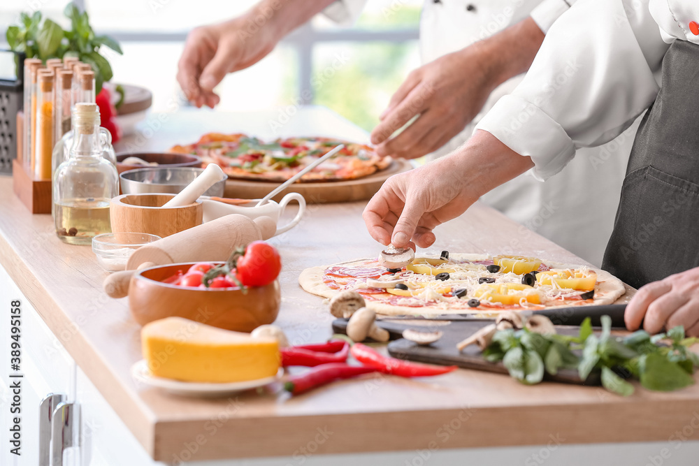 Chefs cooking tasty pizza in kitchen