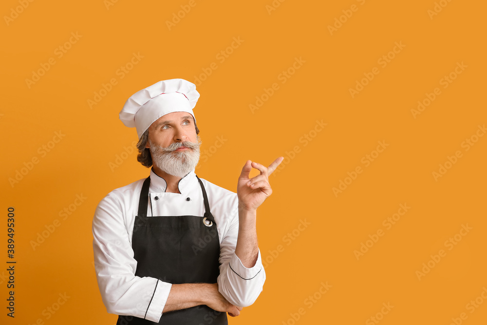 Mature male chef pointing at something on color background