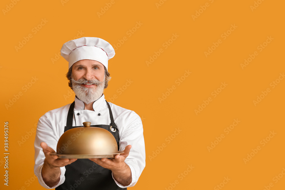 Mature male chef with tray and cloche on color background