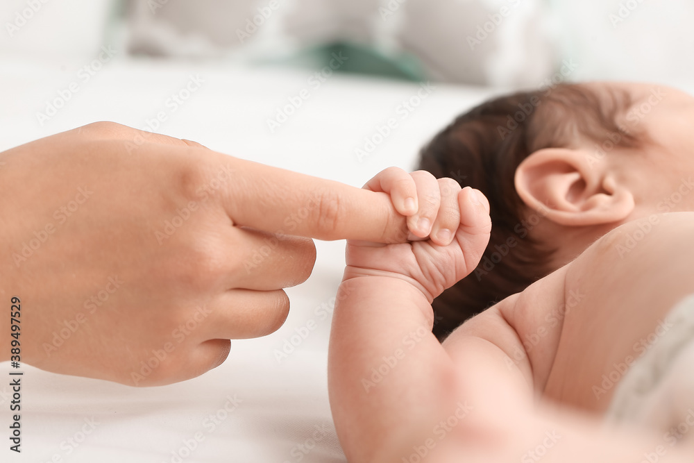 Cute little baby with mothers hand on bed