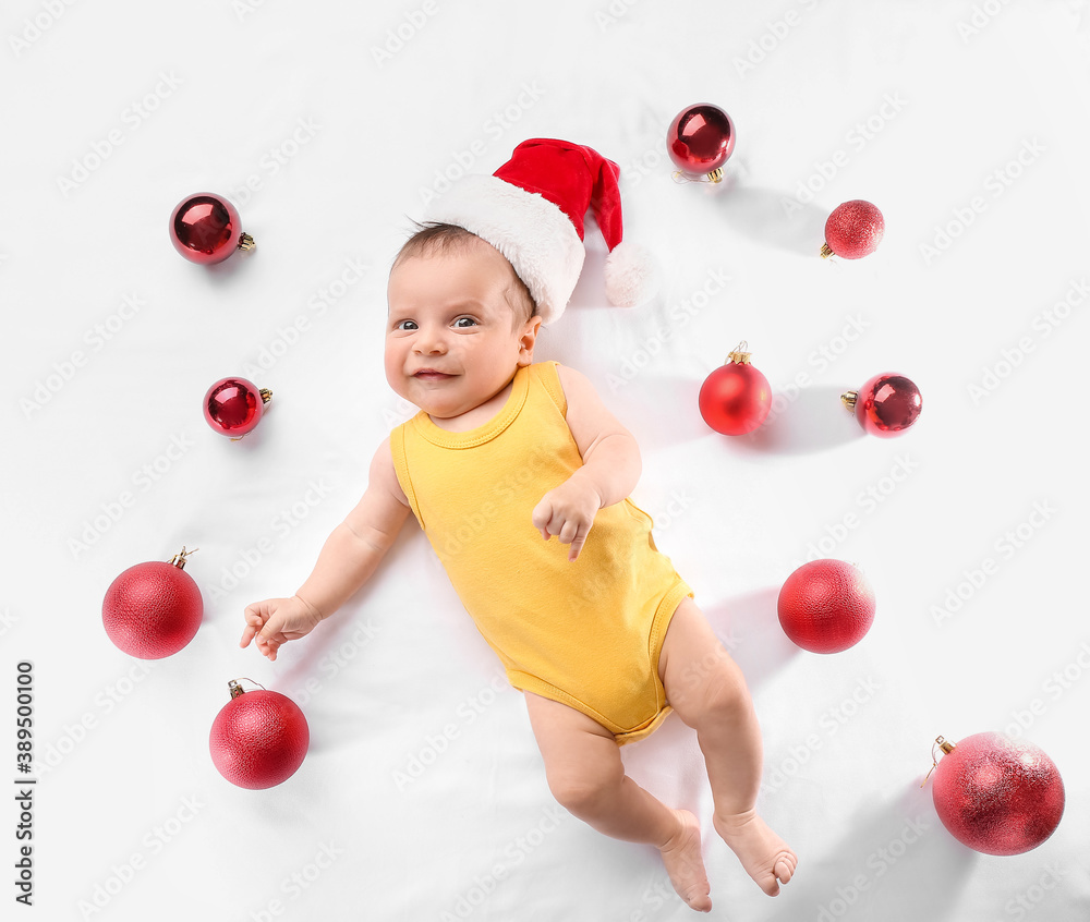 Cute little baby in Santa hat and with Christmas balls on white background