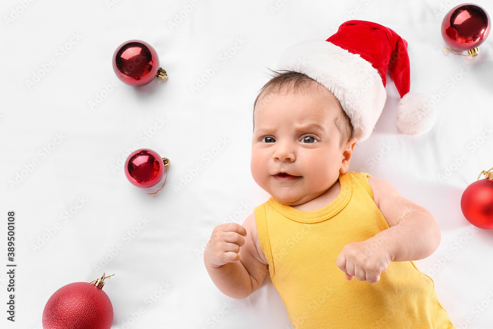 Cute little baby in Santa hat and with Christmas balls on white background