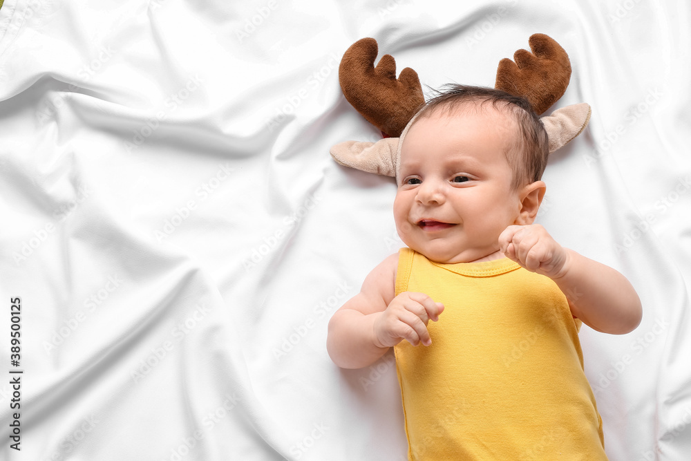 Cute little baby with deer horns lying on bed. Christmas celebration