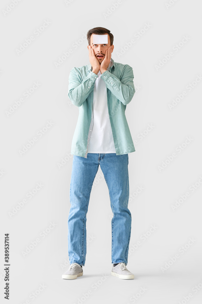 Confused man with blank note paper on his forehead against grey background