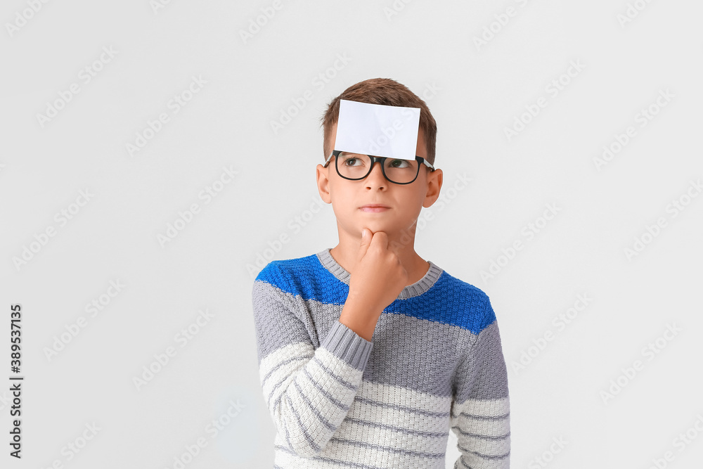 Thoughtful boy with blank note paper on his forehead against light background