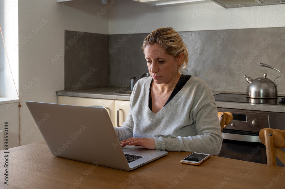 Femme dans sa cuisine en télétravail devant son ordinateur