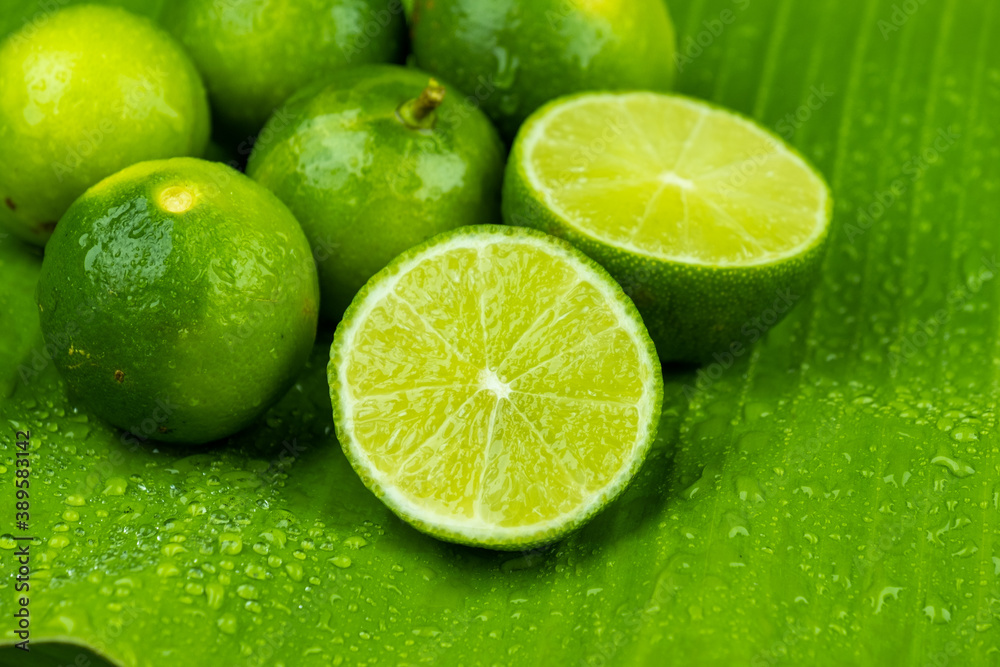 Close up pile of half and whole fresh lime juicy on green banana leaves with clearly water drop on s