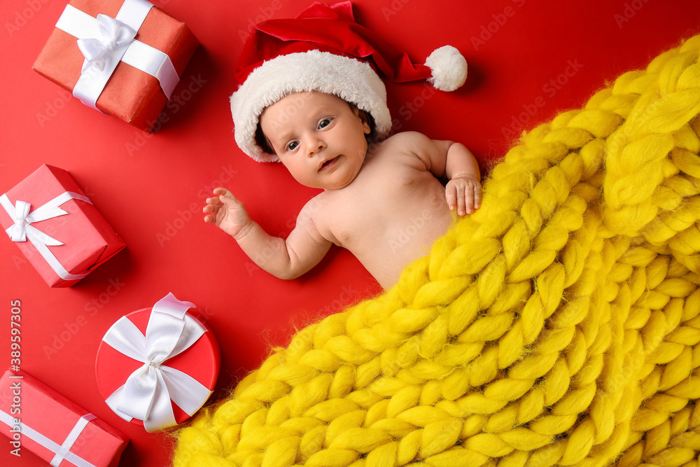 Cute little baby in Santa hat and Christmas gift boxes on color background