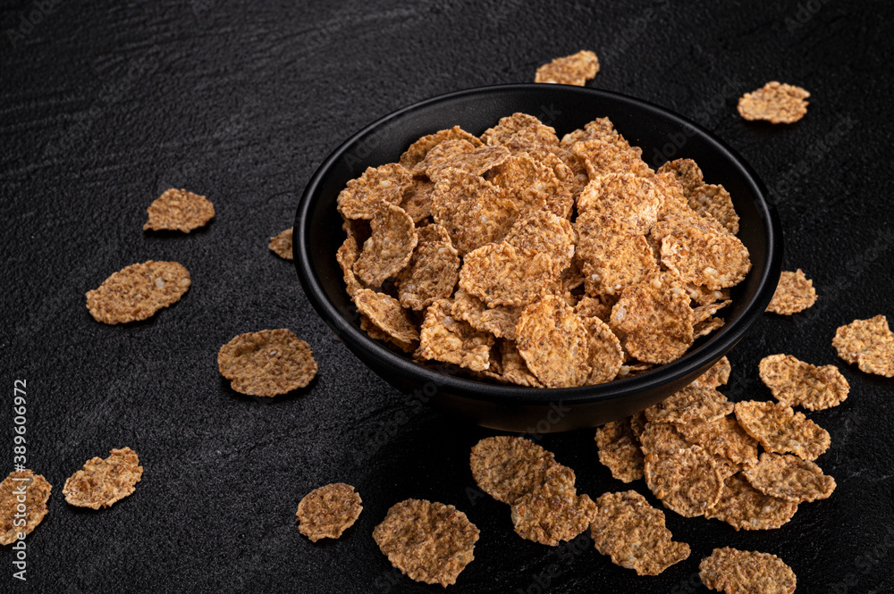 Bran flakes in bowl on black background with copy space