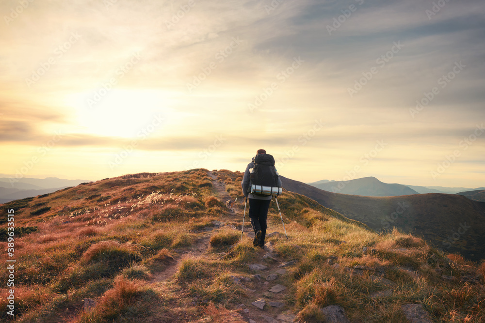 Man backpacker traveling with a dog. Hiker going uphill against scenic sunset sky background