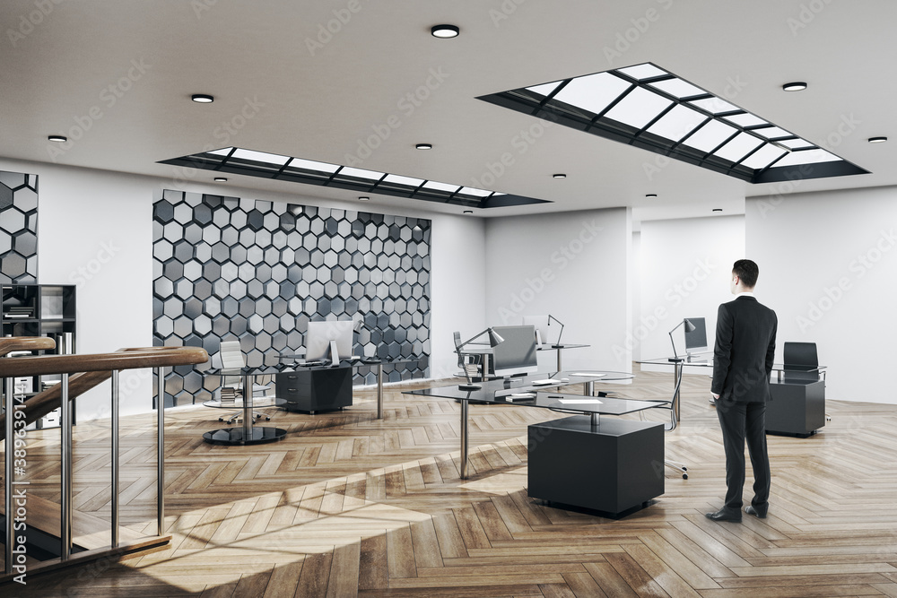 Businessman standing in office interior with blank silver honeycomb wall.