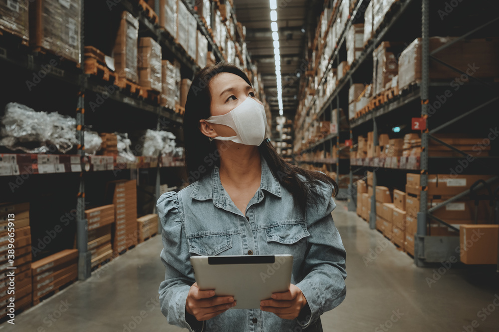 Asian business working woman wear mask using digital tablet checking stock of products in warehouse