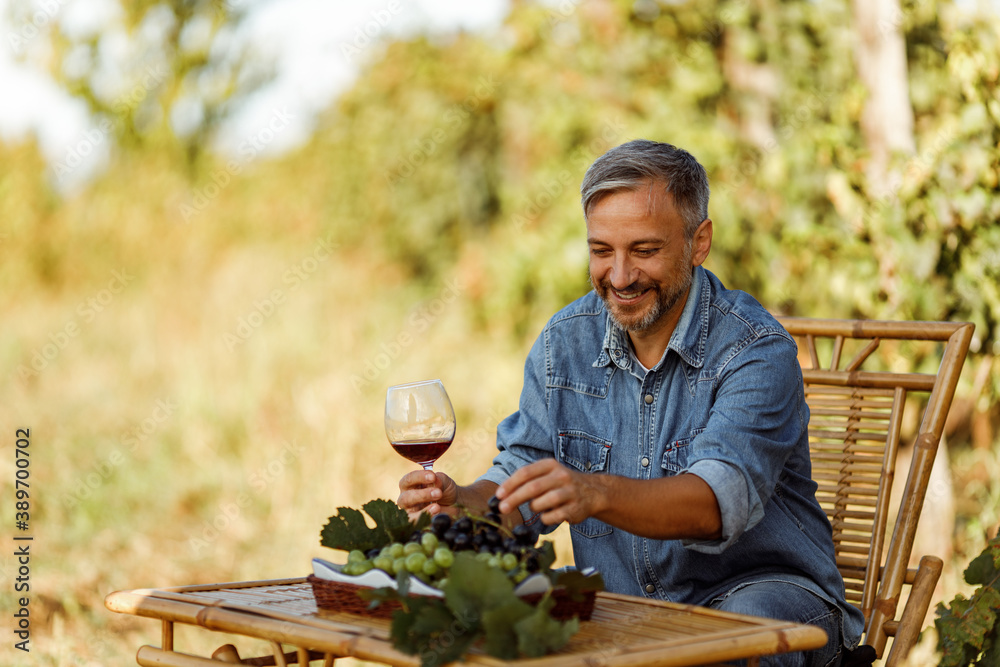 Man eating grapes and holding a glass of red wine from his winery.