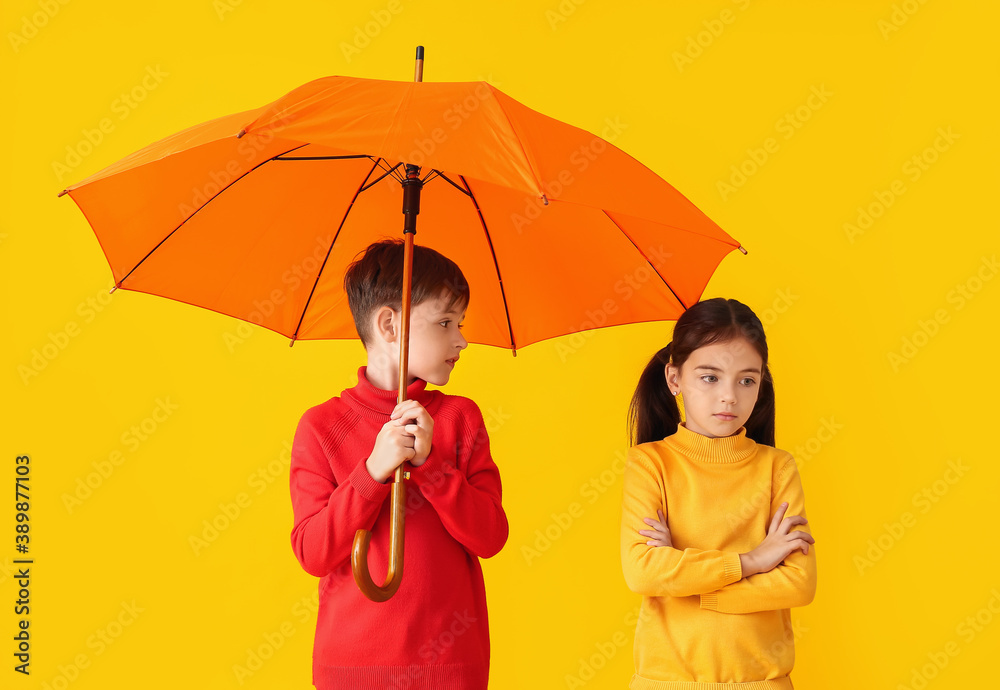 Cute little children in autumn clothes and with umbrella on color background