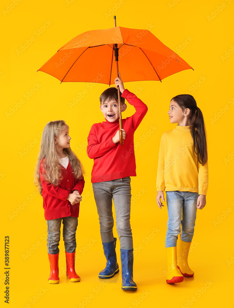 Cute little children in autumn clothes and with umbrella on color background