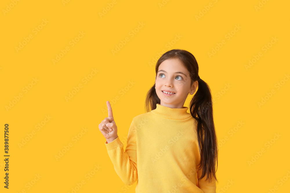 Cute little girl in autumn clothes pointing at something on color background